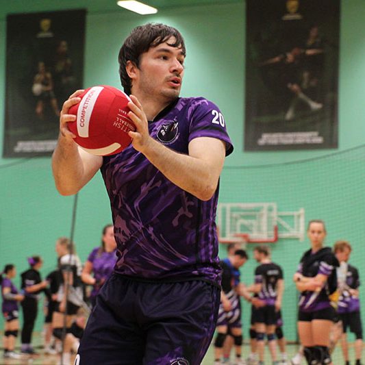 Man holding ball at Surrey Dodgeball with girls playing dodgeball in background